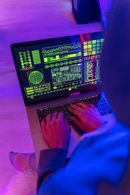 An unrecognizable person using a laptop indoors with digital screens displaying data and analytics.